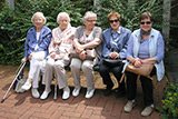 Fnf Teilnehmerinnen des Seniorenausflugs sitzen vor Fahrtbeginn auf der Bank vor der Trinitatiskirche.