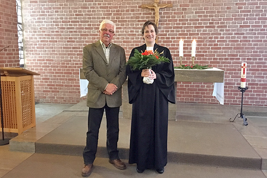 Pfarrerin Mohr und Heinz Rau stehen vor dem Altar der Trinitatiskirche, wo der stellvertretende Vorsitzende des Kirchenvorstands der Pfarrerin einen Blumenstrau berreicht hat.
